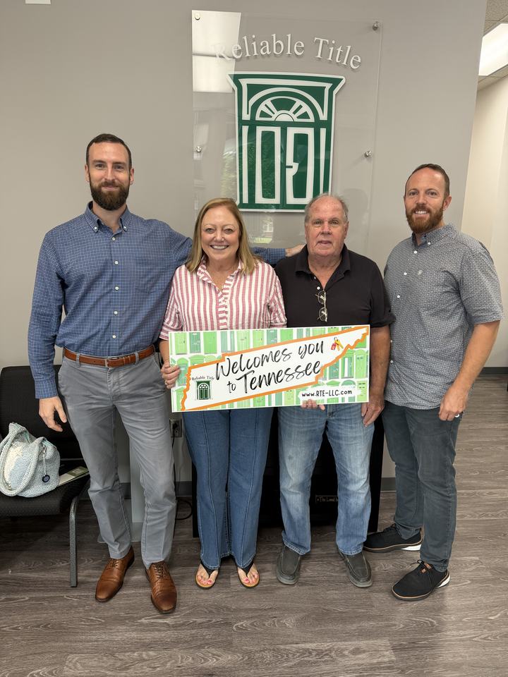Sam Timlick with a realtor and clients holding a "Welcomes You to Tennessee" sign at a home closing